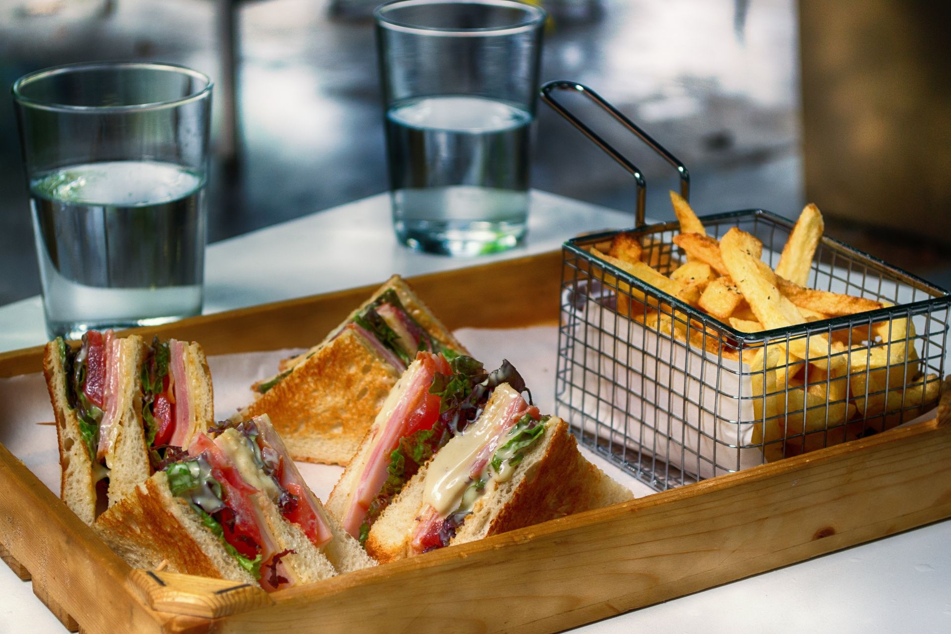 Grilled sandwiches, french fries in a wire basket, and glasses of water on a wooden tray.